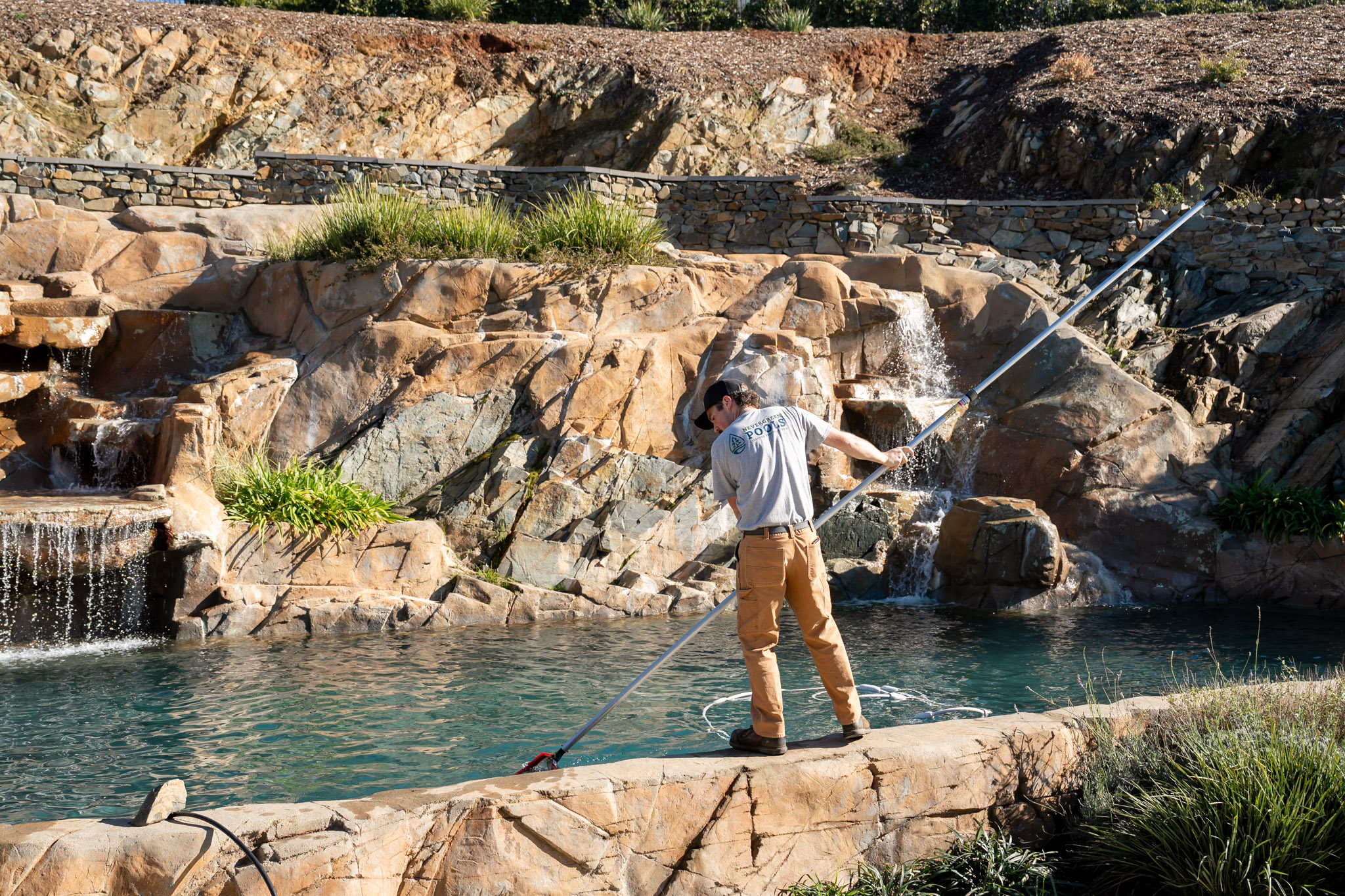 Vintage Pool Service tech brushing and vacuuming a pool